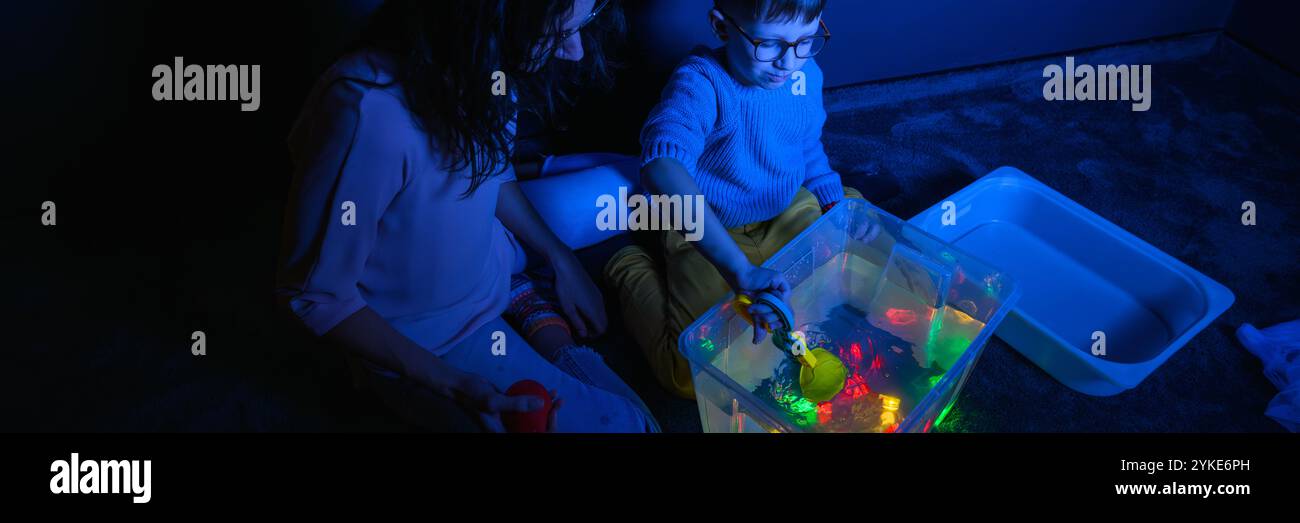 Bambino e terapista in camera stimolante sensoriale, Black snoezelen. Bambino autistico che gioca con il terapista durante la sessione di terapia occupazionale. Foto Stock