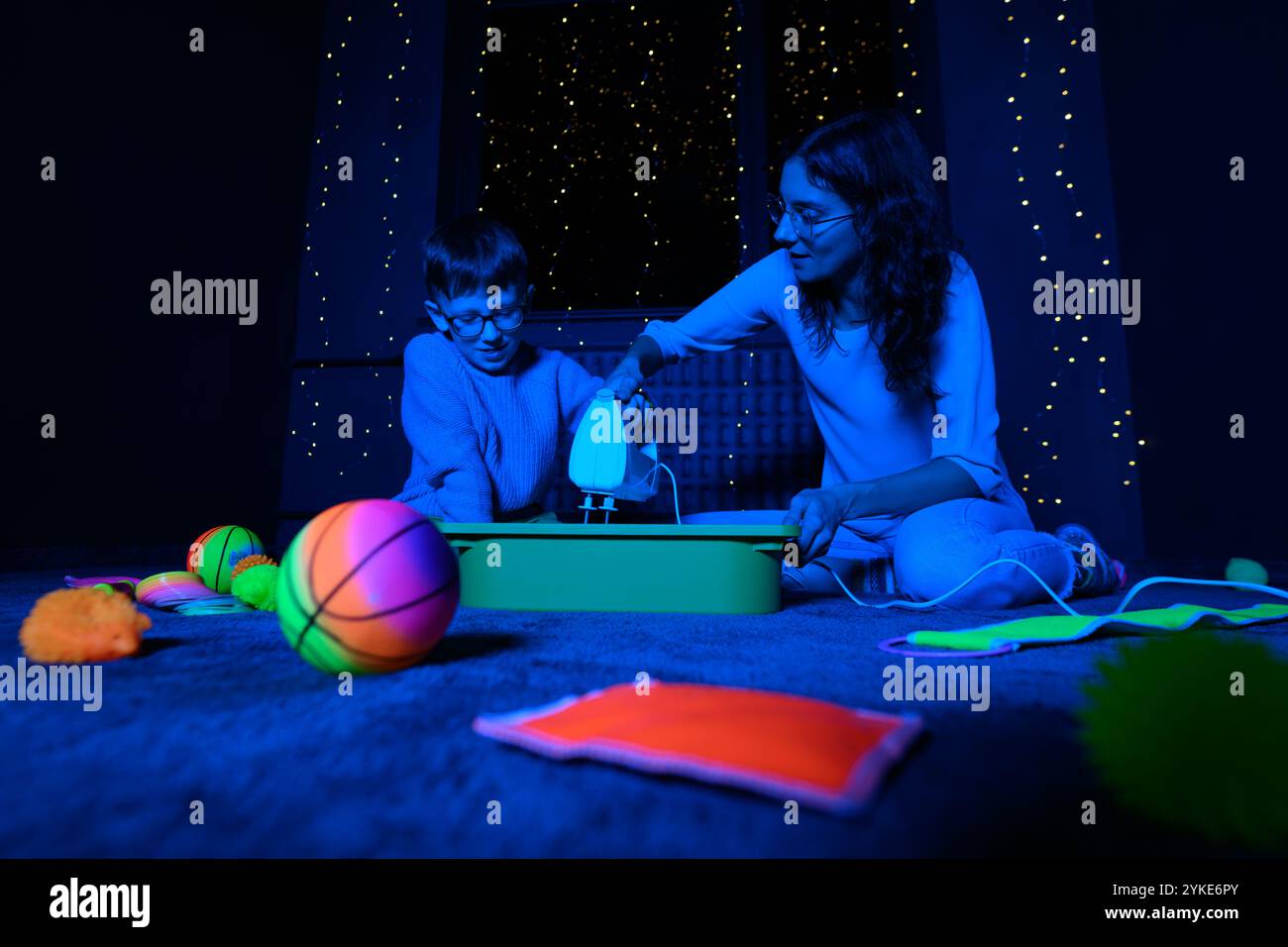 Bambino e terapista in camera stimolante sensoriale, Black snoezelen. Bambino autistico che gioca con il terapista durante la sessione di terapia occupazionale. Foto Stock