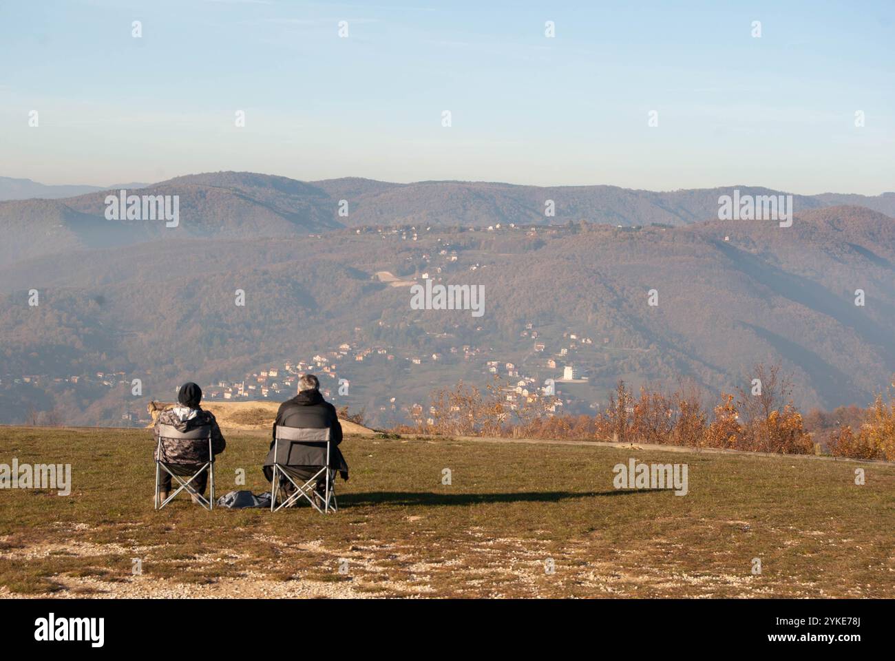 Una allegra coppia di anziani che cammina su una collina, crogiolandosi alla luce del sole sulle sedie pieghevoli. Foto Stock