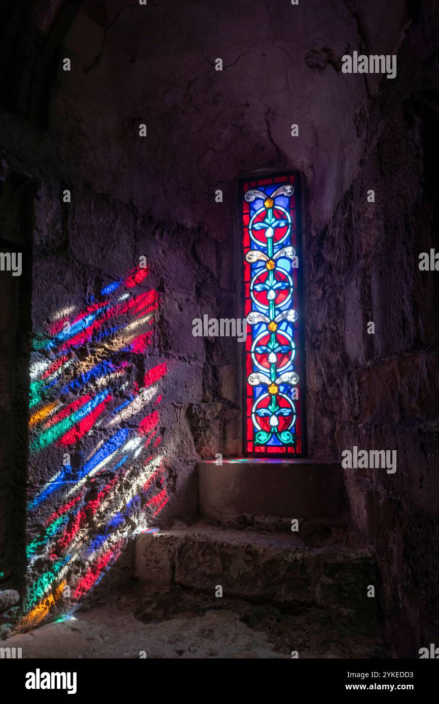 Una finestra di vetro colorato con il sole che splende creando ombre colorate su un muro di pietra Foto Stock