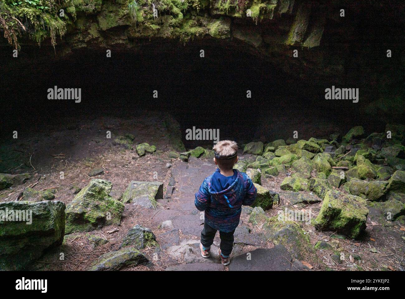 Un ragazzo guarda giù le scale di roccia verso l'apertura di una grotta Foto Stock