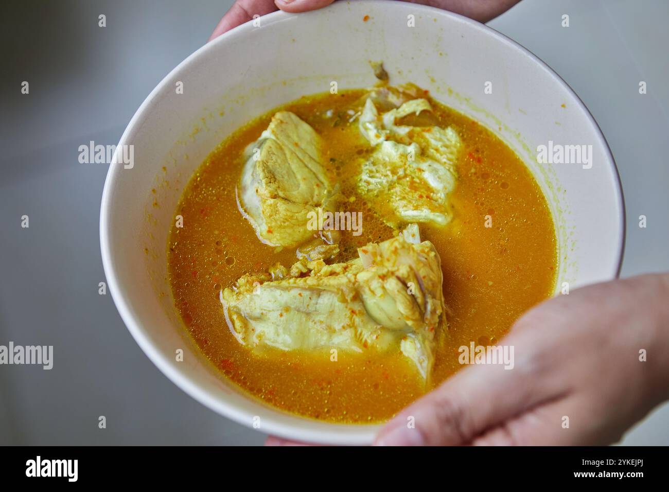 Mano tagliata che tiene la zuppa acida con pesce dentice nel recipiente Foto Stock