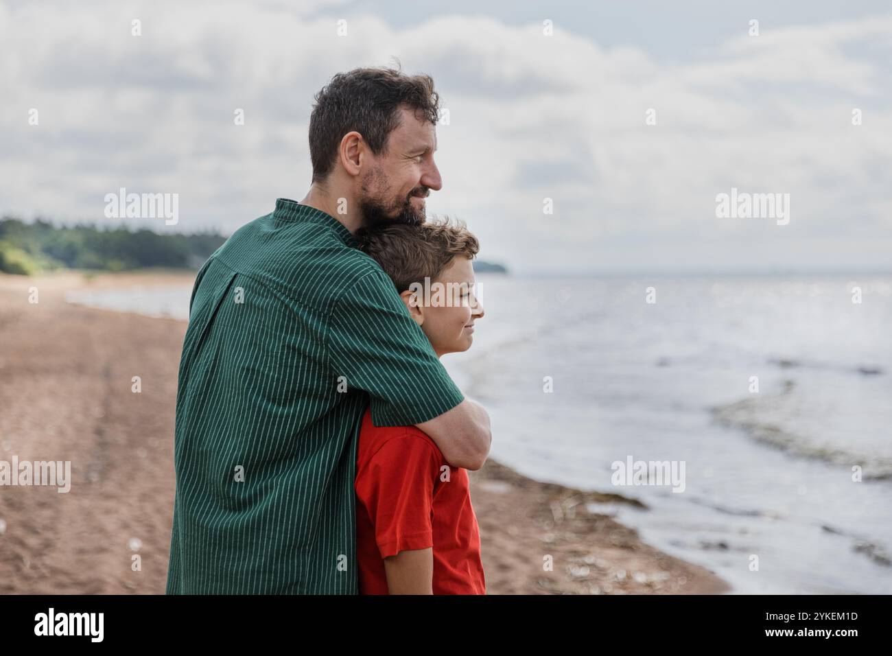 Padre e figlio adolescente camminano e guardano insieme il mare abbracciando Foto Stock