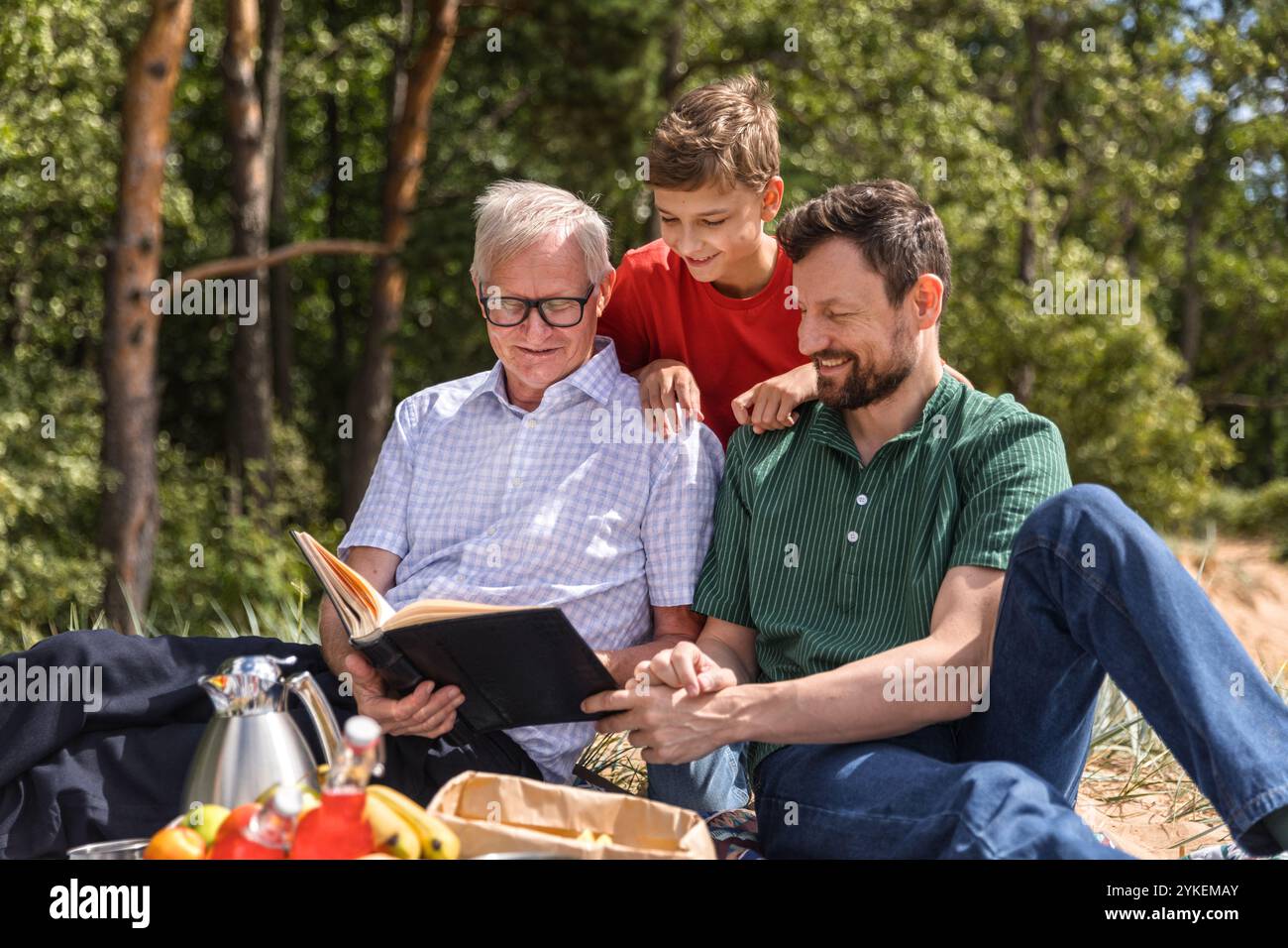 L'uomo anziano, il ragazzo adolescente e suo padre guardano un album fotografico al picnic Foto Stock