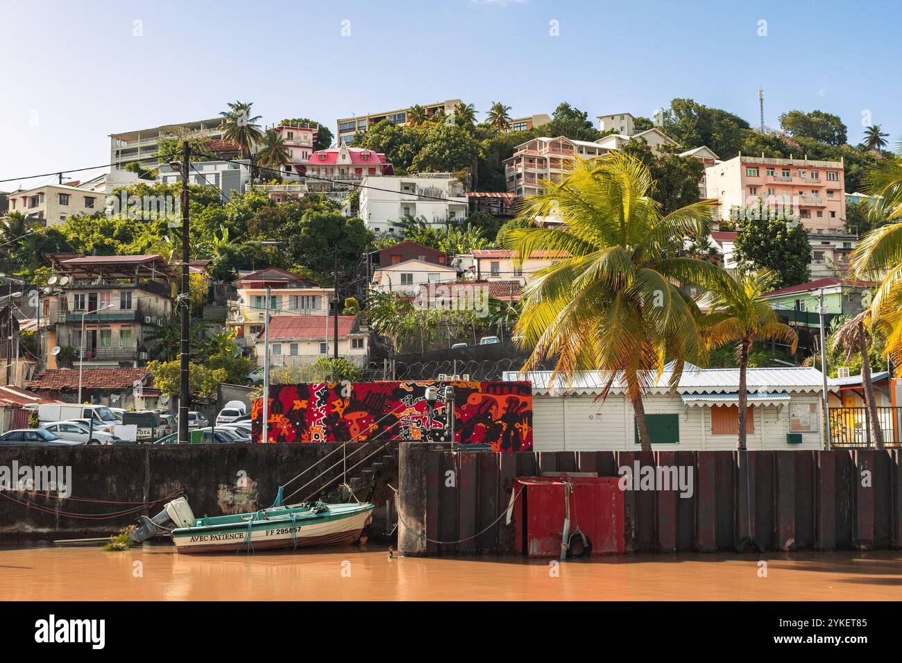 Fort-de-France, Martinica - 3 gennaio 2018: Edifici colorati si arrampicano sulla collina che si affaccia su un tranquillo porto. Le barche riposano pacificamente, riflettendo la V Foto Stock