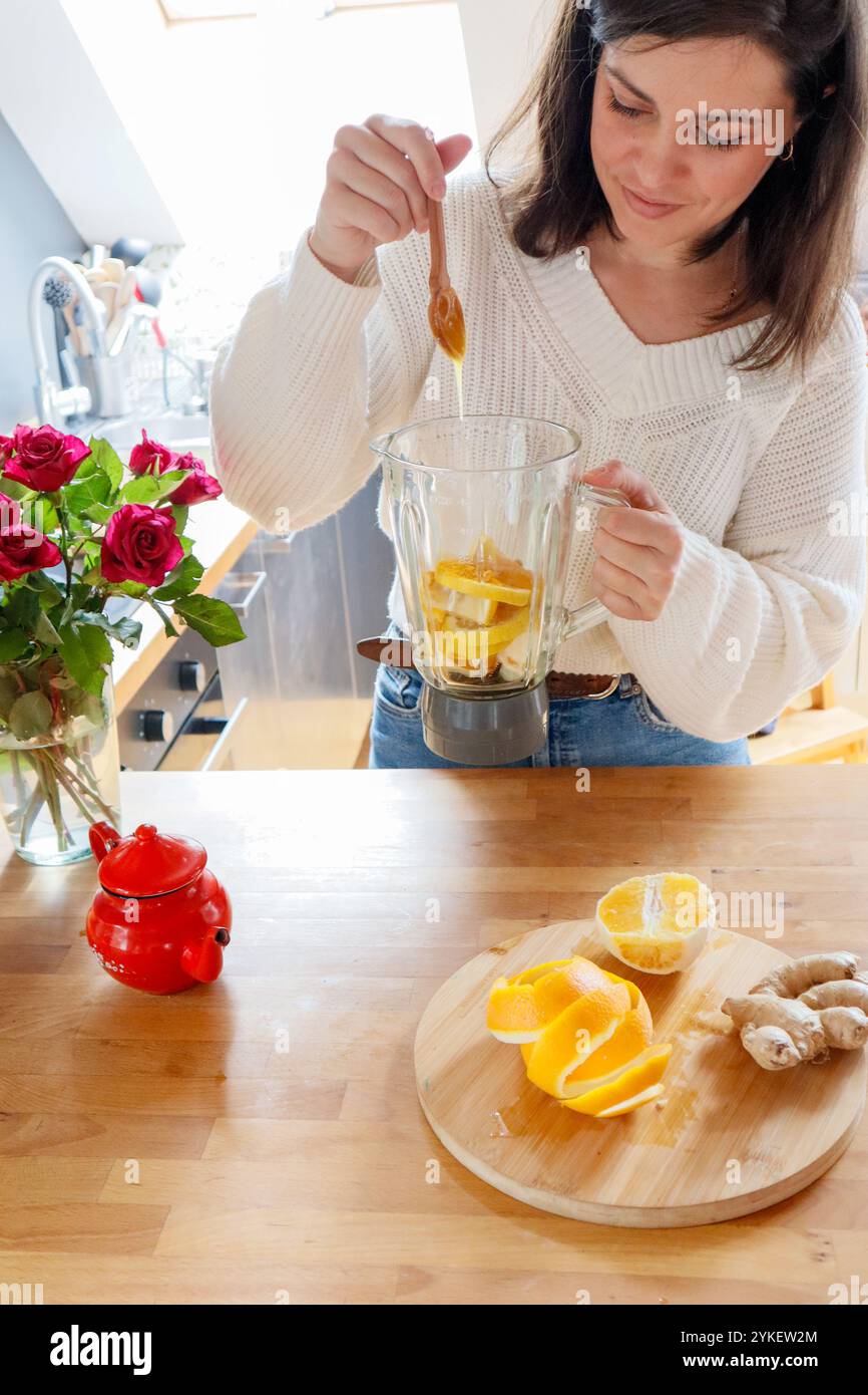 Donna che aggiunge miele al frullatore con arancia e zenzero per il tè Foto Stock