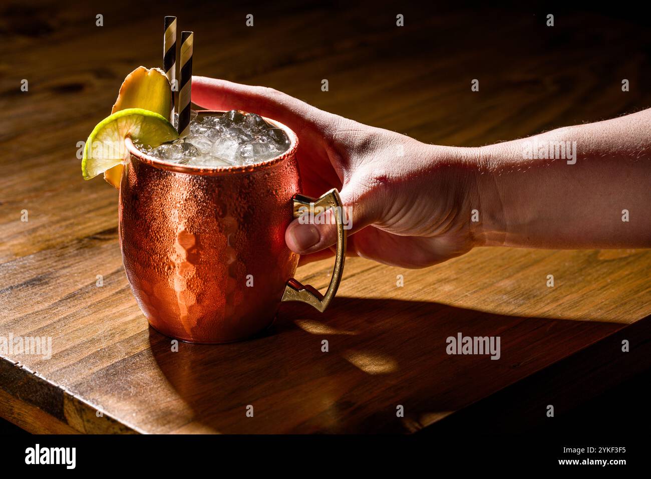 Un Moscow Mule servito in una classica tazza di rame, guarnita con lime e menta, appoggiato su un rustico tavolo in legno, perfetto per gli amanti dei cocktail e il bar- Foto Stock
