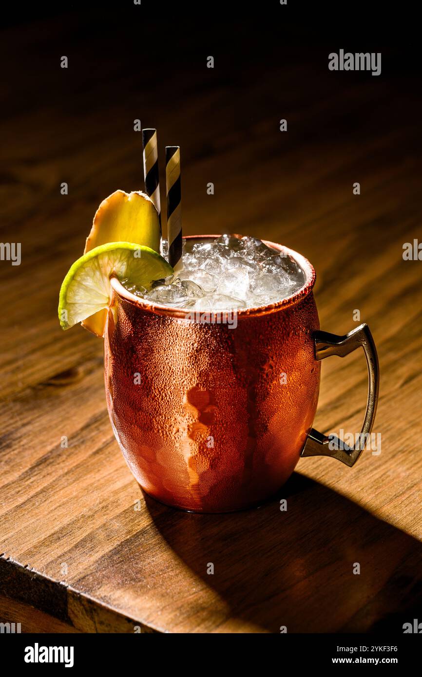 Un rinfrescante mulo di Mosca servito in una classica tazza di rame, decorato con lime fresco e zenzero, la bevanda ghiacciata brilla sotto una luce calda, evidenziando Foto Stock