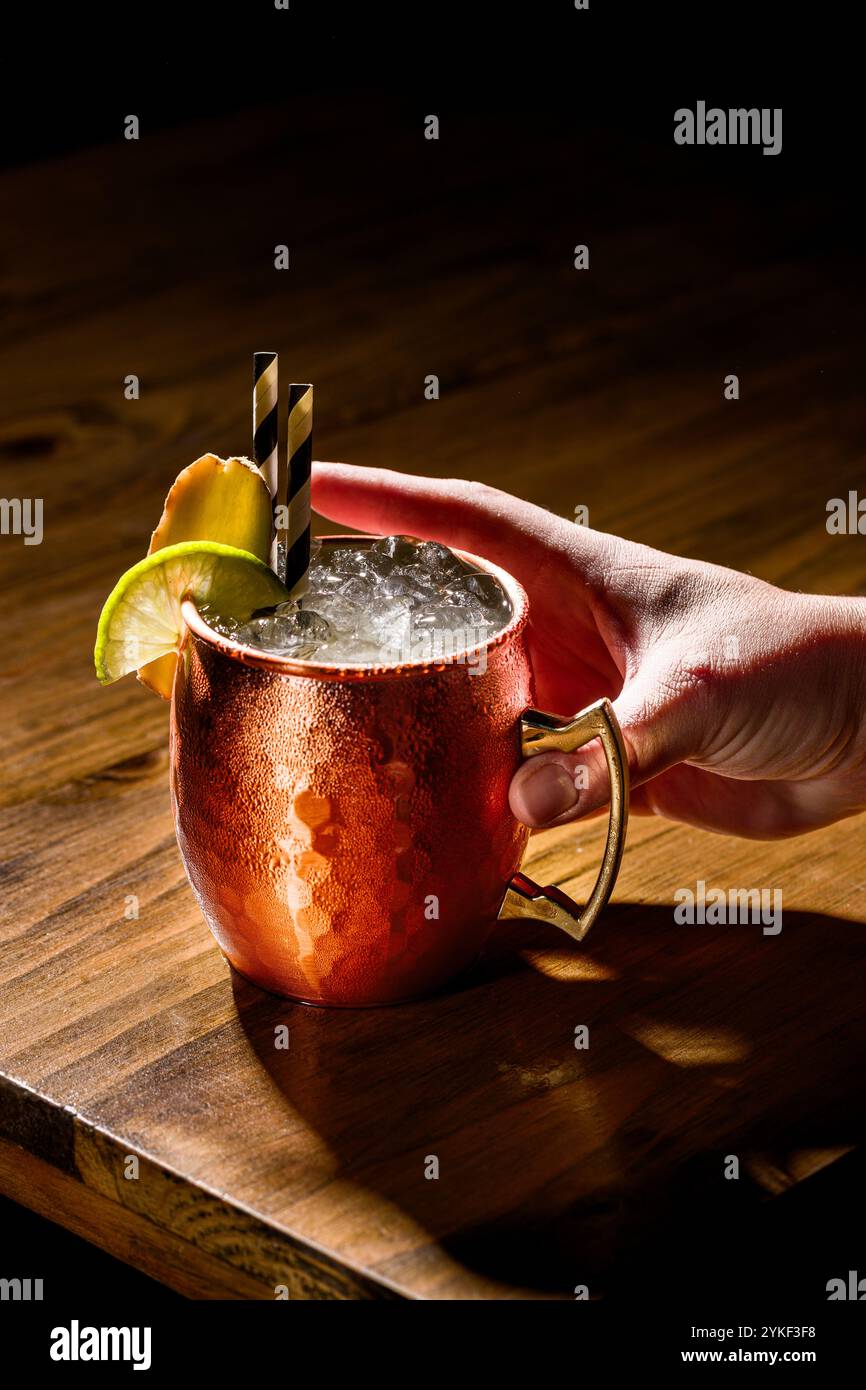 Un Moscow Mule servito in una classica tazza di rame, guarnita con lime e menta, appoggiato su un rustico tavolo in legno, perfetto per gli amanti dei cocktail e il bar- Foto Stock