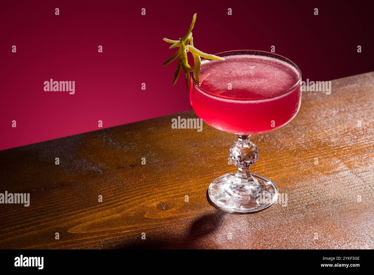 Un classico cocktail cosmopolita elegantemente presentato in vetro con stelo di cristallo, decorato con un tocco di lime, perfetto per menu bar, guide cocktail o. Foto Stock