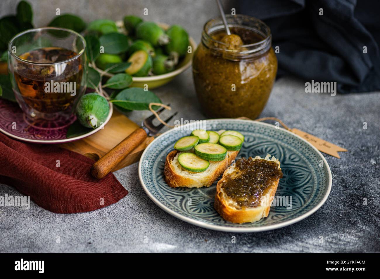 Un ambiente tranquillo con tè floreale e panini adornati con marmellata di feijoa fatta in casa e fette di cetriolo fresco accanto ad esso, un barattolo di ricca marmellata di feijoa Foto Stock