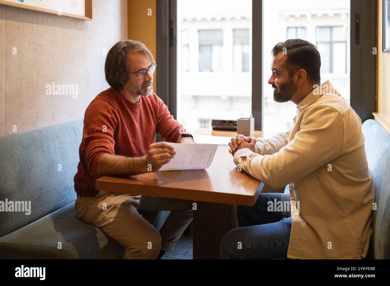 Due professionisti stanno discutendo in un moderno spazio di coworking, si siedono uno di fronte all'altro a un tavolo di legno, scambiandosi idee, aga Foto Stock