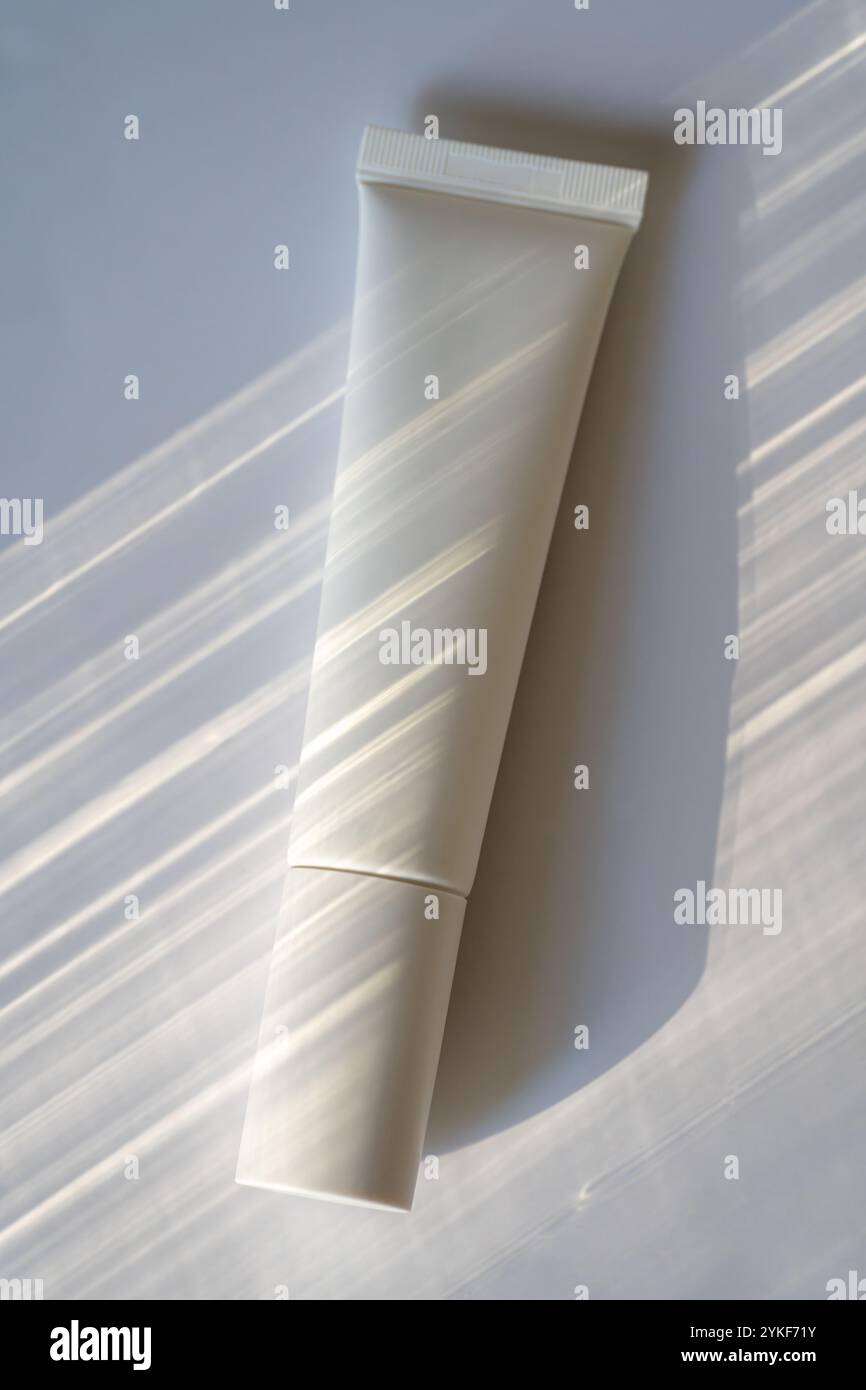 Vista dall'alto di un tubo cosmetico senza marchio inondato di luce naturale con linee d'ombra distinte, che creano un'estetica morbida e minimalista ideale per bea Foto Stock