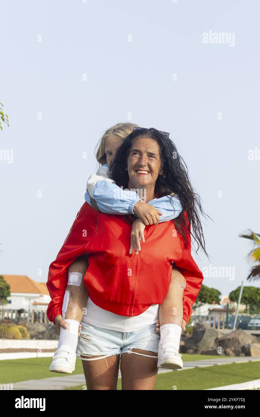 Un'immagine che sorride raffigurante una donna sorridente in una giacca rossa che trasporta sua figlia con la sindrome di Stuve-Wiedemann, entrambi gli individui che mostrano resili Foto Stock