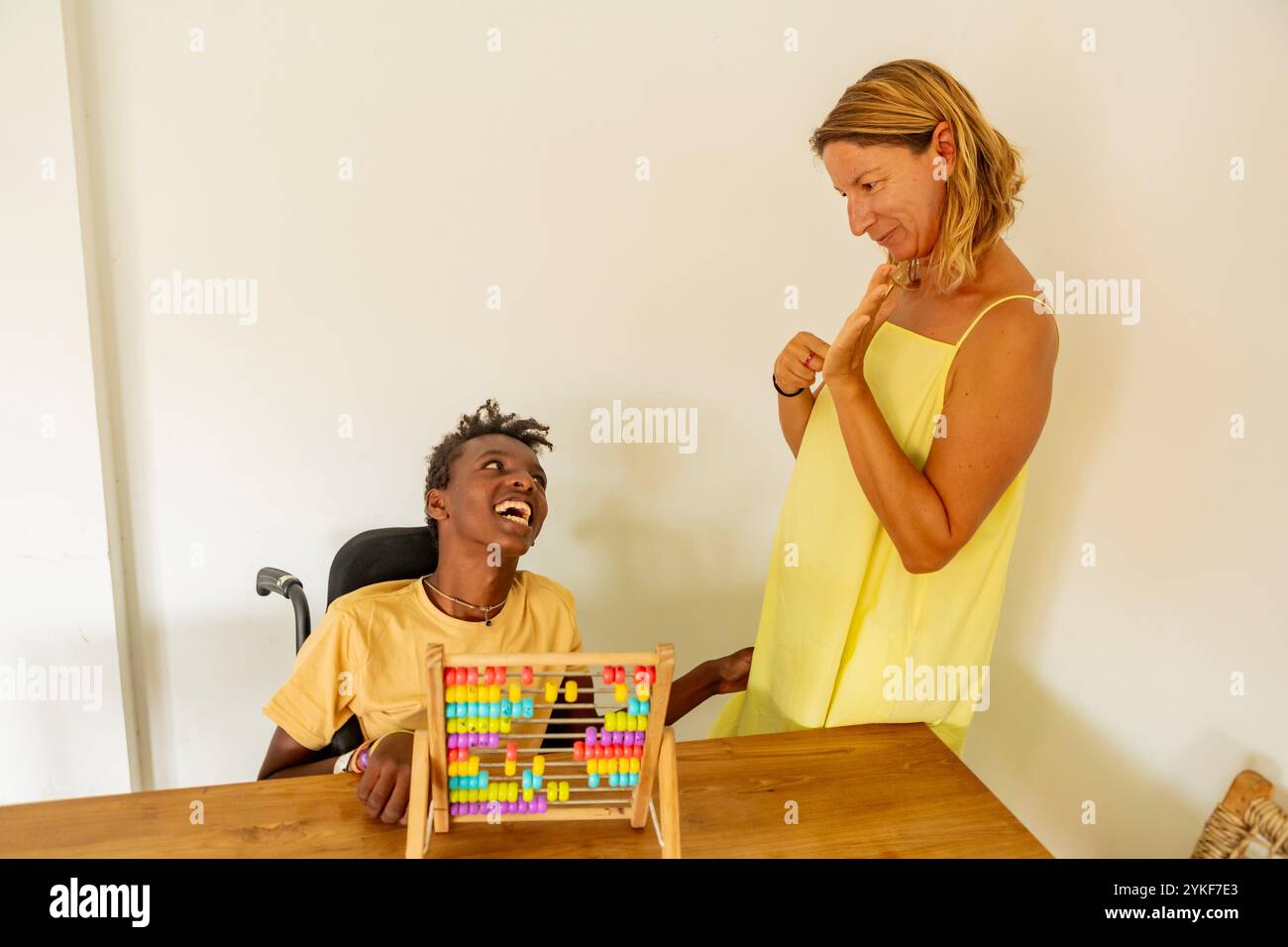 Un giovane ragazzo nero gioioso con paralisi cerebrale si impegna con colorate perline di abaco durante una divertente sessione di apprendimento con la sua insegnante caucasica a. Foto Stock