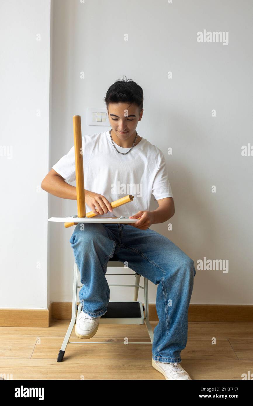 Un uomo trans sorridente assembla una sedia di legno nel suo nuovo appartamento, simboleggiando un nuovo inizio e la fiducia in se stesso all'interno della comunità LGBTQIA+ Foto Stock