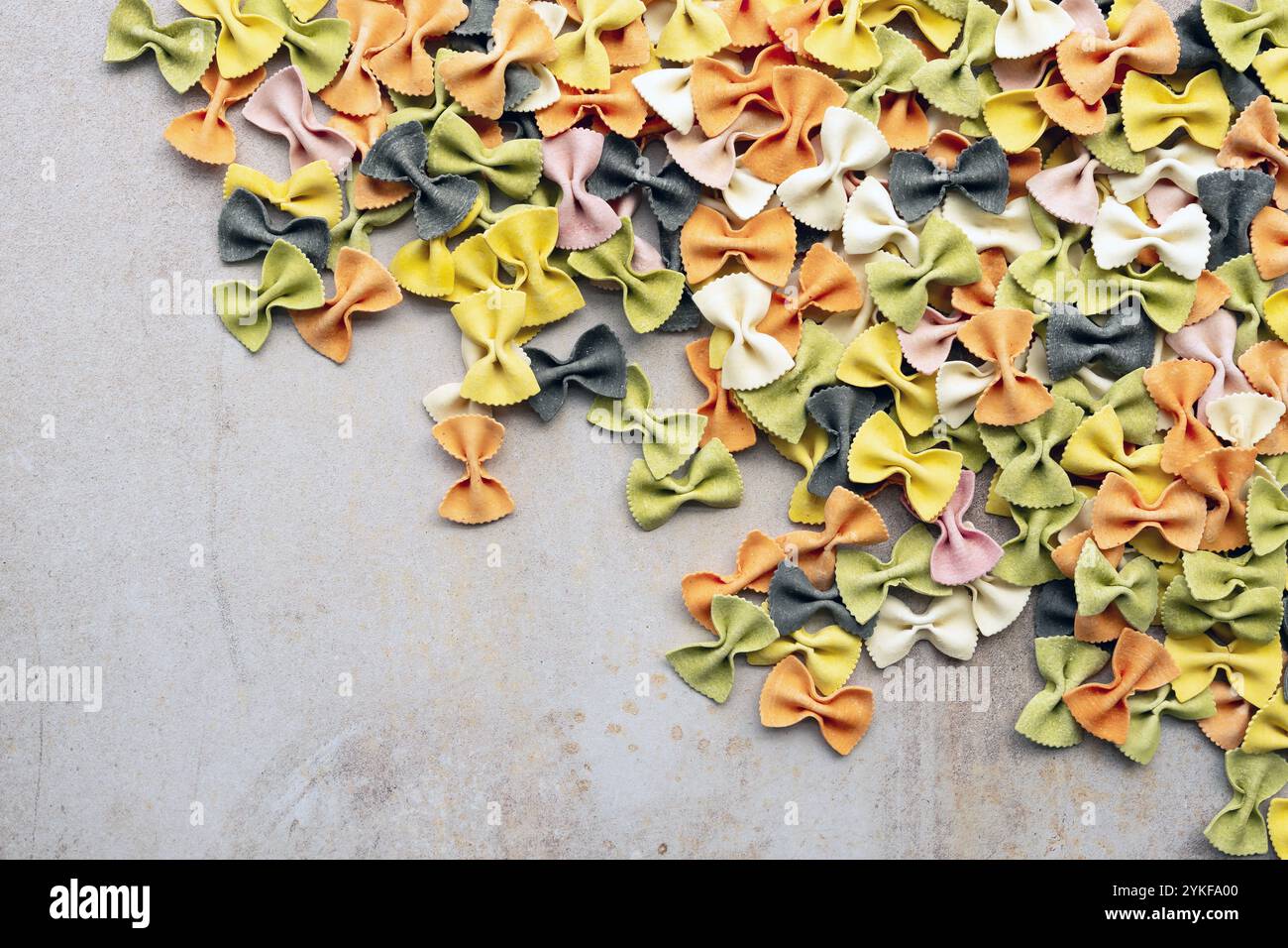 Vista dall'alto della pasta multicolore alle farfalle fatta con ingredienti naturali come curcuma, spinaci, barbabietole, paprika e inchiostro di calamaro, sparso su un testo Foto Stock