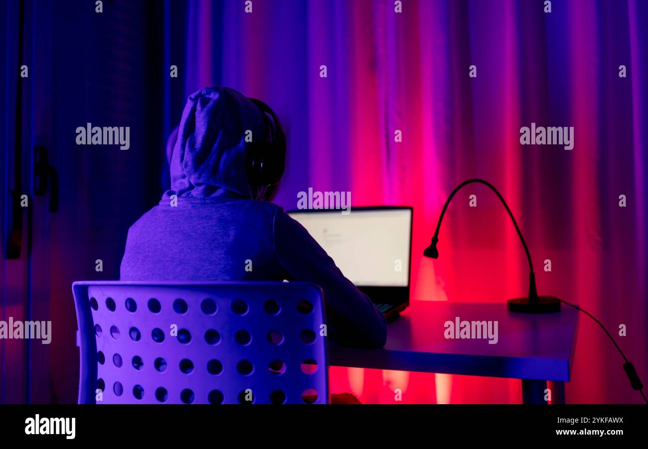 Vista posteriore di un ragazzo irriconoscibile impegnato nel trading online. L'immagine presenta una vivace retroilluminazione multicolore che aggiunge un'atmosfera dinamica al Foto Stock