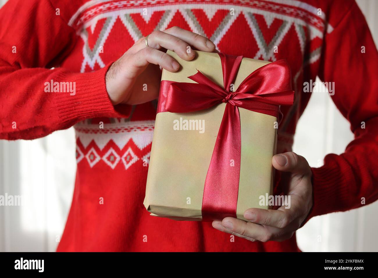 Uomo in maglione rosso natalizio con confezione regalo confezionata in carta artigianale con nastro rosso. Stagione delle vacanze. Foto Stock