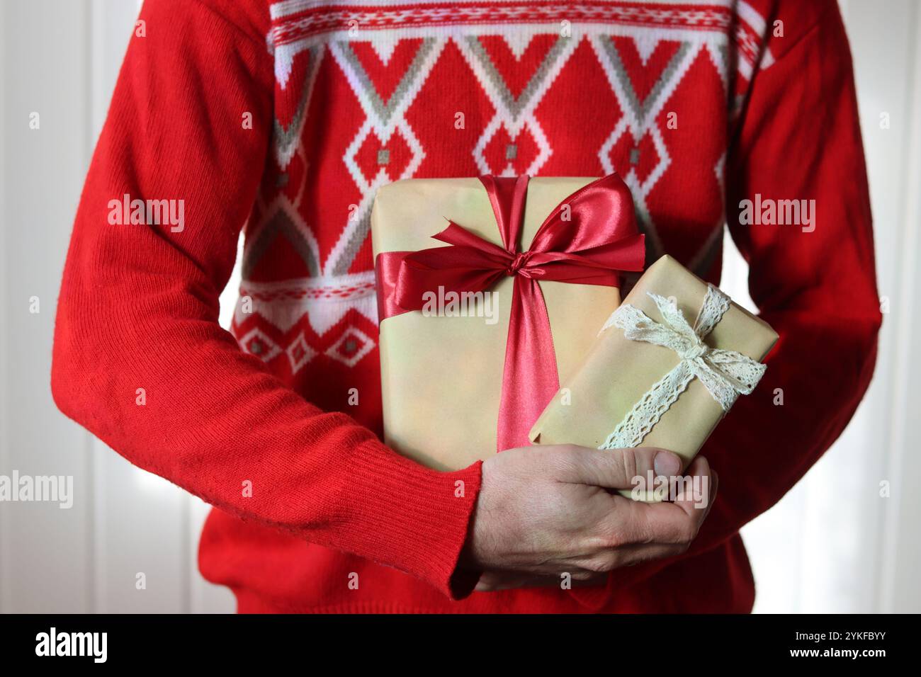 Uomo in maglione rosso natalizio con confezione regalo confezionata in carta artigianale con nastro rosso. Stagione delle vacanze. Foto Stock
