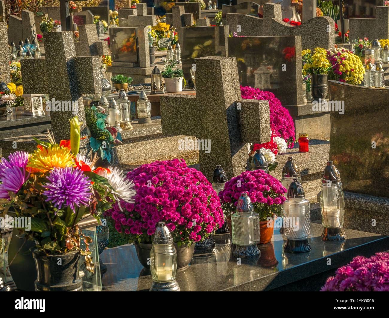 Un tranquillo cimitero con vivaci composizioni floreali e candele accese che creano un'atmosfera tranquilla. Le lapidi in marmo sono circondate da fiori colorati Foto Stock