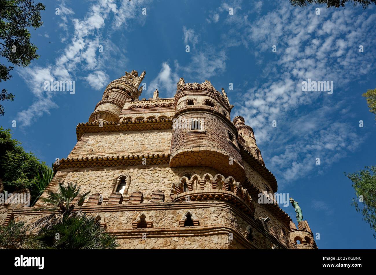 Vista verso l'alto del castello di Colomares, le sue intricate opere in pietra e le torri gotiche su un vivace cielo blu Foto Stock