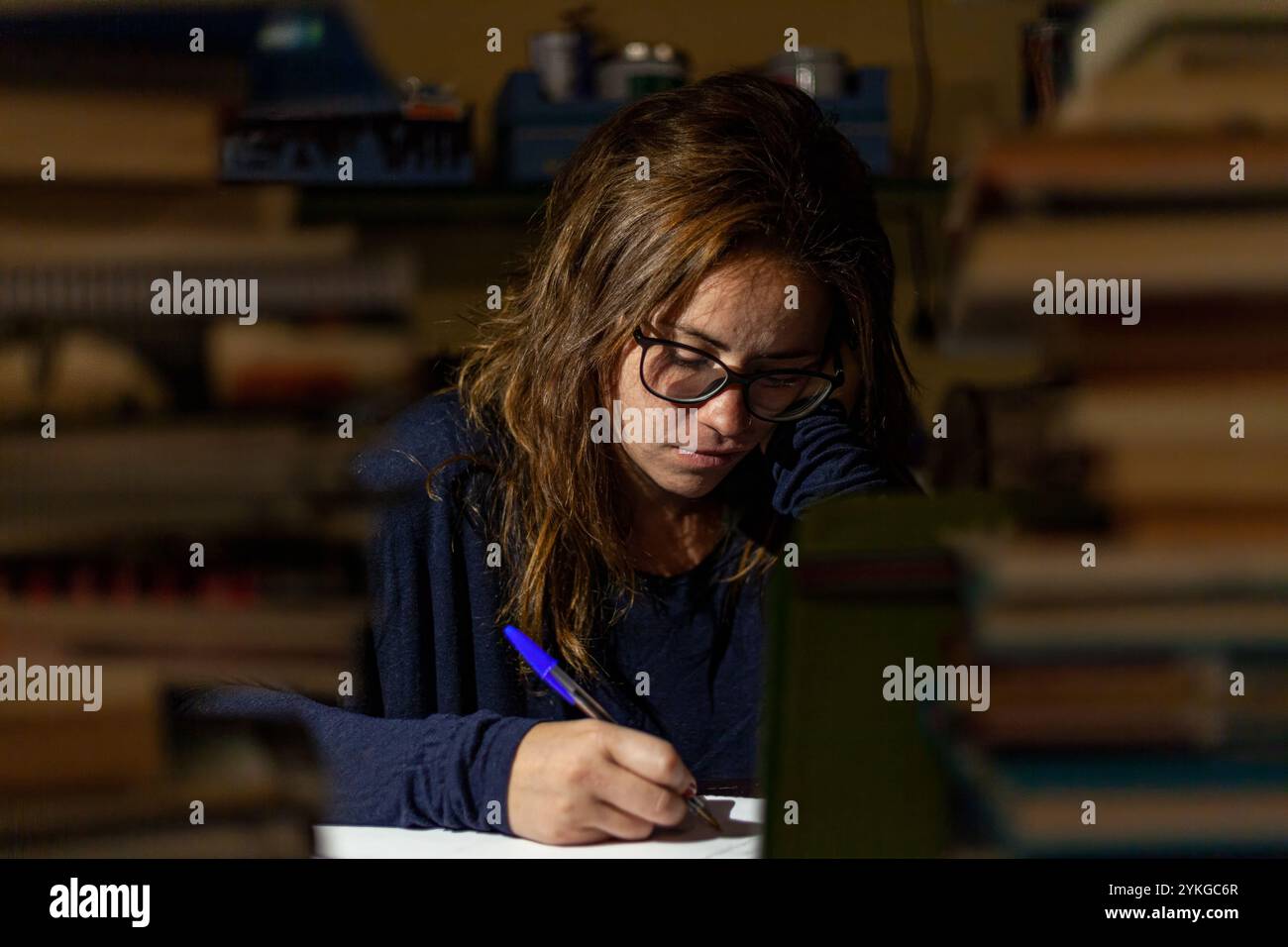 Studente giovane concentrato con occhiali che studia per gli esami in una biblioteca di notte Foto Stock
