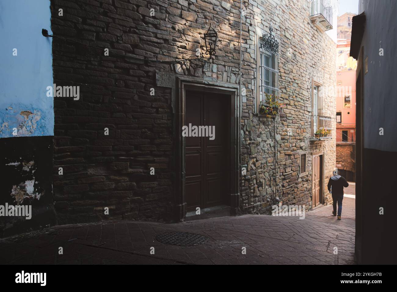 Guanajuato, Messico - 6 febbraio 2024: Una figura solitaria cammina lungo uno stretto vicolo acciottolato nella città vecchia di Guanajuato, Messico, circondato da texture Foto Stock