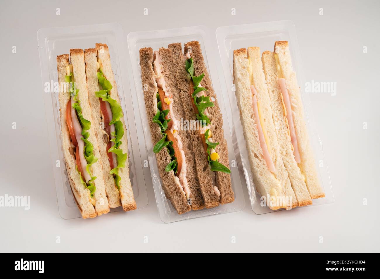 Tre panini confezionati con pane bianco e integrale, ripieni di lattuga, pomodori, tacchino, formaggio, prosciutto e verdure. Ideale per pasti veloci. Foto Stock