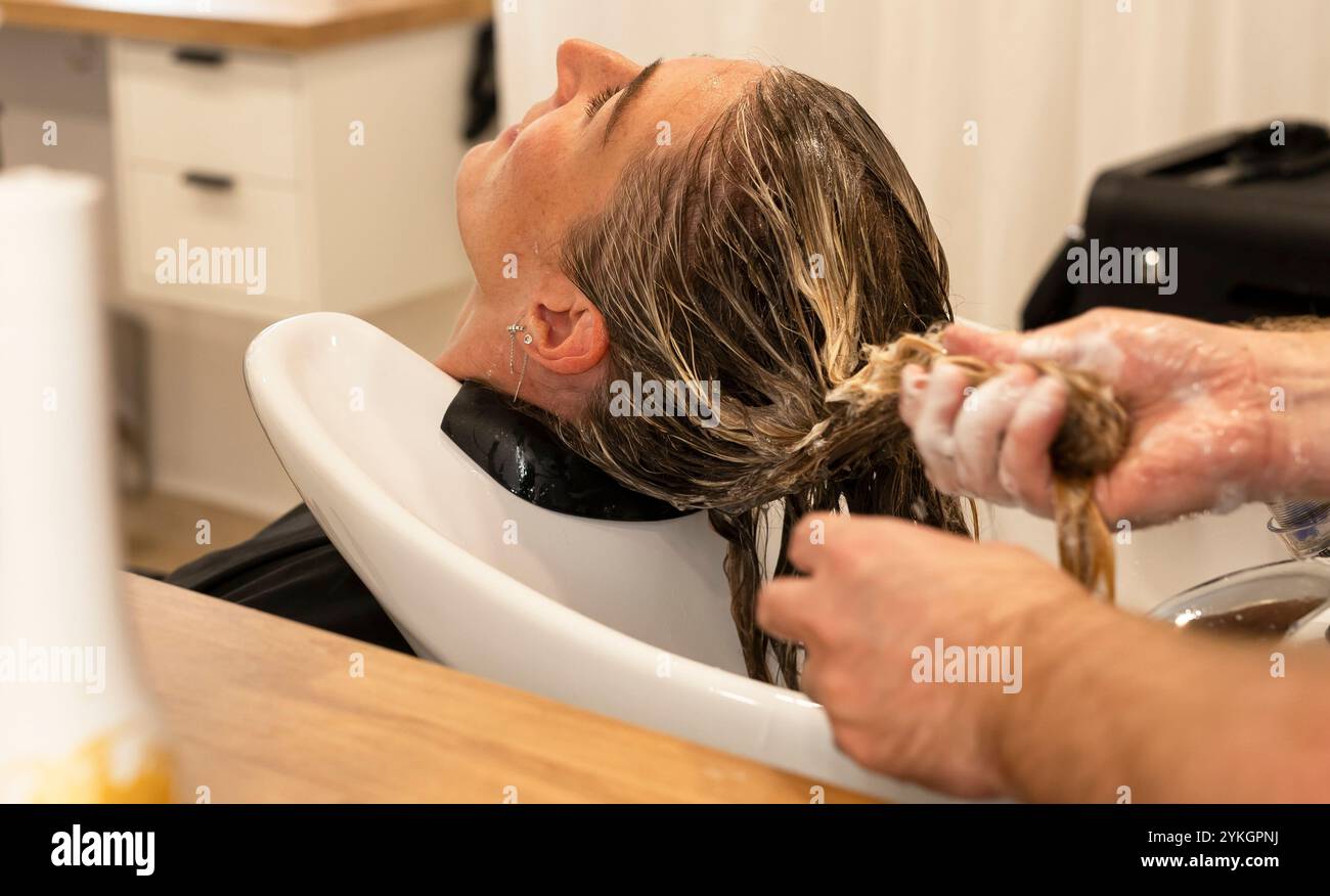 Friseur macht Foliensträhnen bei einer jungen Frau. Il parrucchiere strizza i capelli di una giovane donna Foto Stock