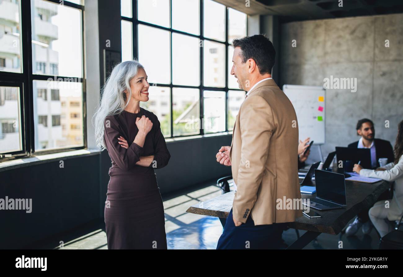 Due colleghi discutono idee in un ufficio moderno con grandi finestre Foto Stock