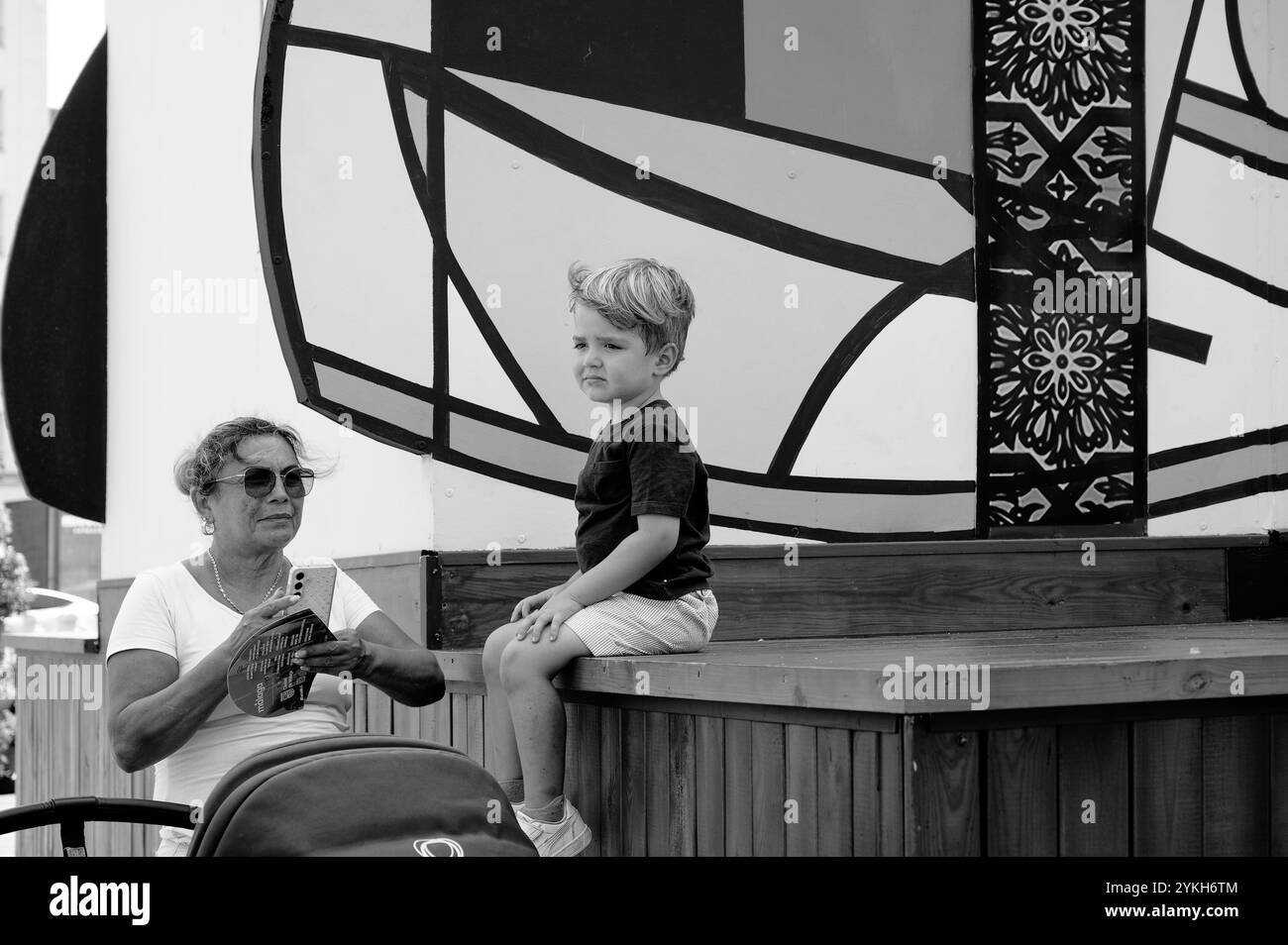 La babysitter guarda il bambino seduto su una piattaforma di legno sullo sfondo di un'arte astratta in bianco e nero Foto Stock