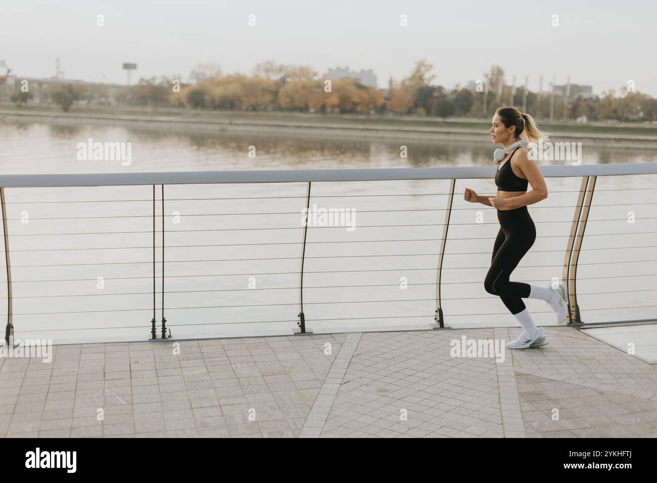 Un determinato corridore procede con sicurezza lungo un sentiero lungo il fiume, abbracciando l'aria frizzante del mattino, con lo skyline della città e gli alberi autunnali che offrono un'immagine Foto Stock