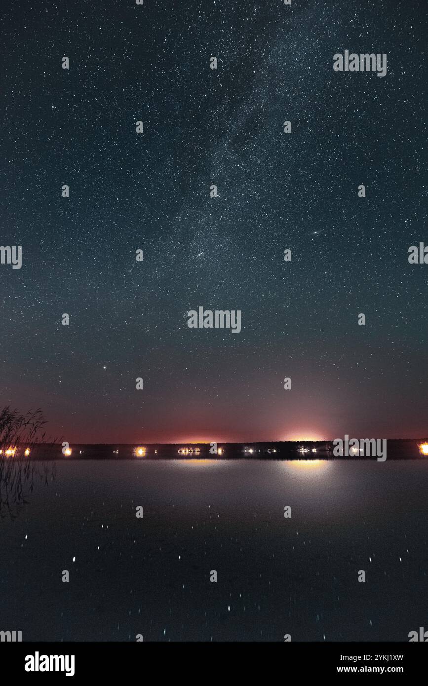 Un cielo notturno mozzafiato pieno di stelle e la via Lattea si riflette su un lago calmo, con lontane luci della città all'orizzonte che creano un ambiente sereno Foto Stock