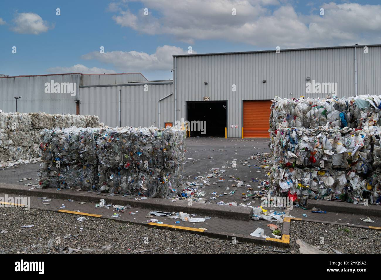 Bottiglie e cartoni di latte in plastica usati che sono stati raggruppati in balle impilate e pronti per il riciclaggio presso un impianto industriale di riciclaggio dei rifiuti di plastica Foto Stock
