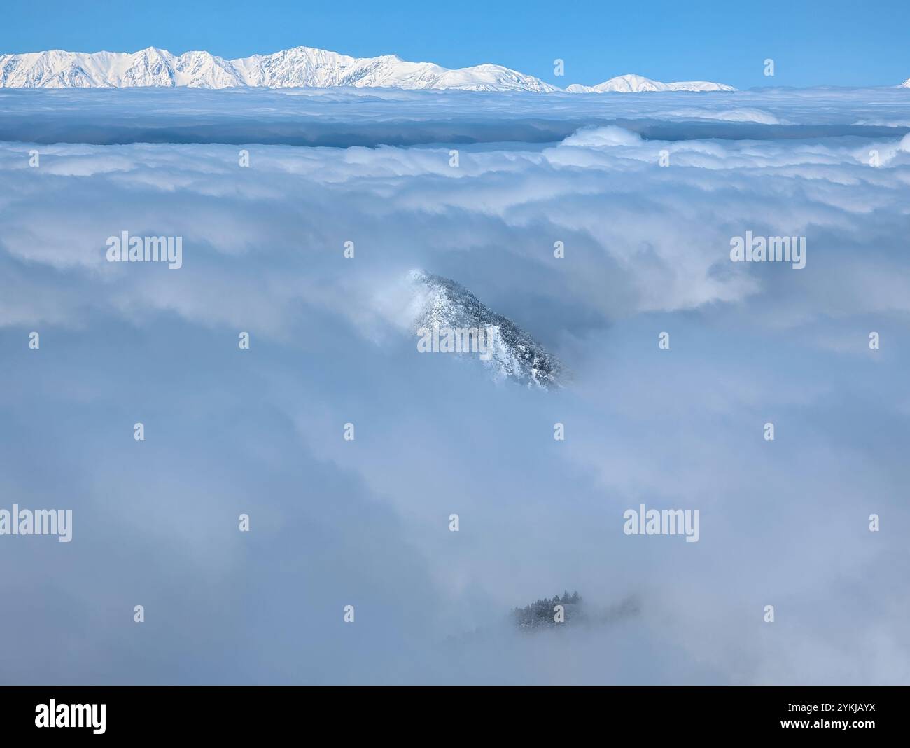 Montagne frastagliate ricoperte di neve che emergono attraverso uno spesso strato di nuvole Foto Stock