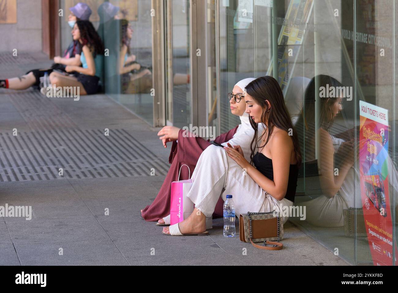 Due ragazze sedute sul pavimento in una piazza di Segovia. Foto Stock
