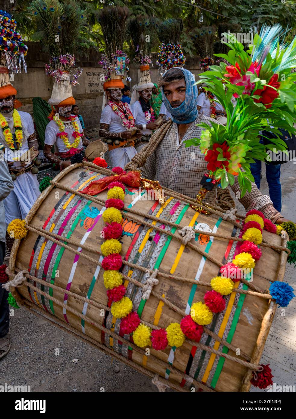 L'uomo mascherato suona un grande tamburo colorato in una processione festosa, circondato da persone in abbigliamento tradizionale Foto Stock