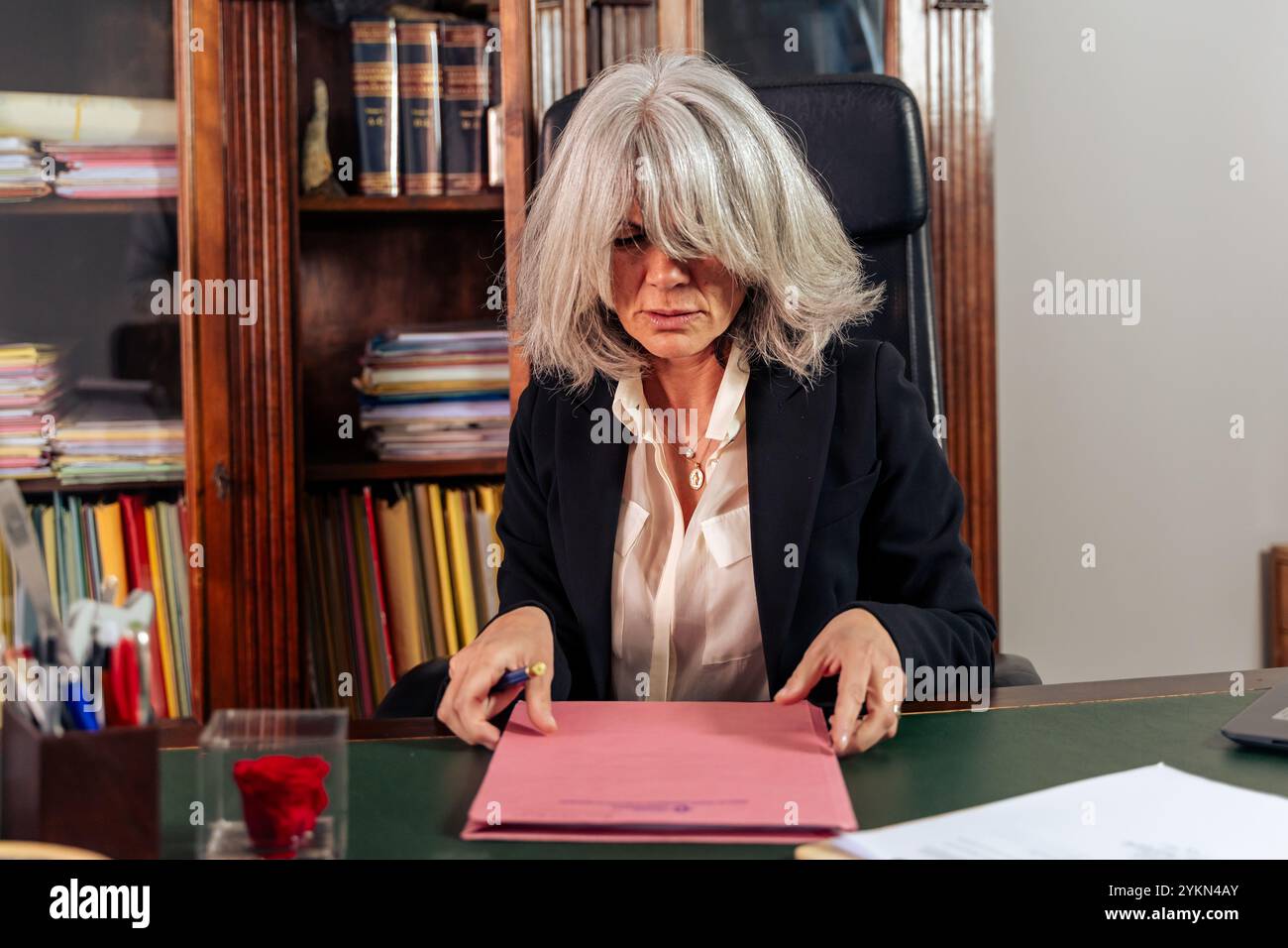 Dirigente femminile con capelli argentati che esamina documenti aziendali critici in un ufficio elegante, con un leader professionale che prende decisioni importanti Foto Stock