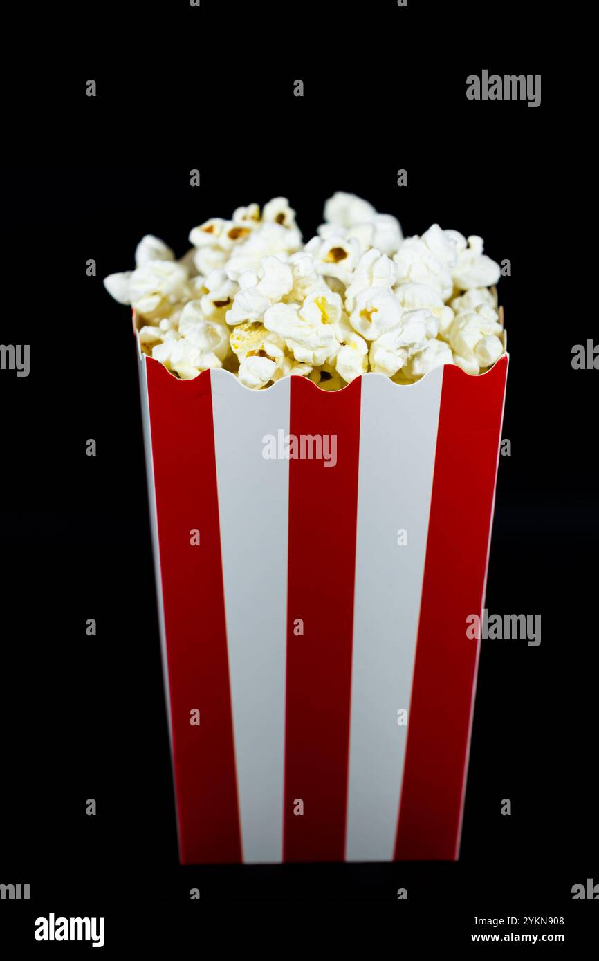 Popcorn in un secchio di cartone rosso con immagine verticale bianca su sfondo nero, concetto di intrattenimento e cibo da cinema Foto Stock