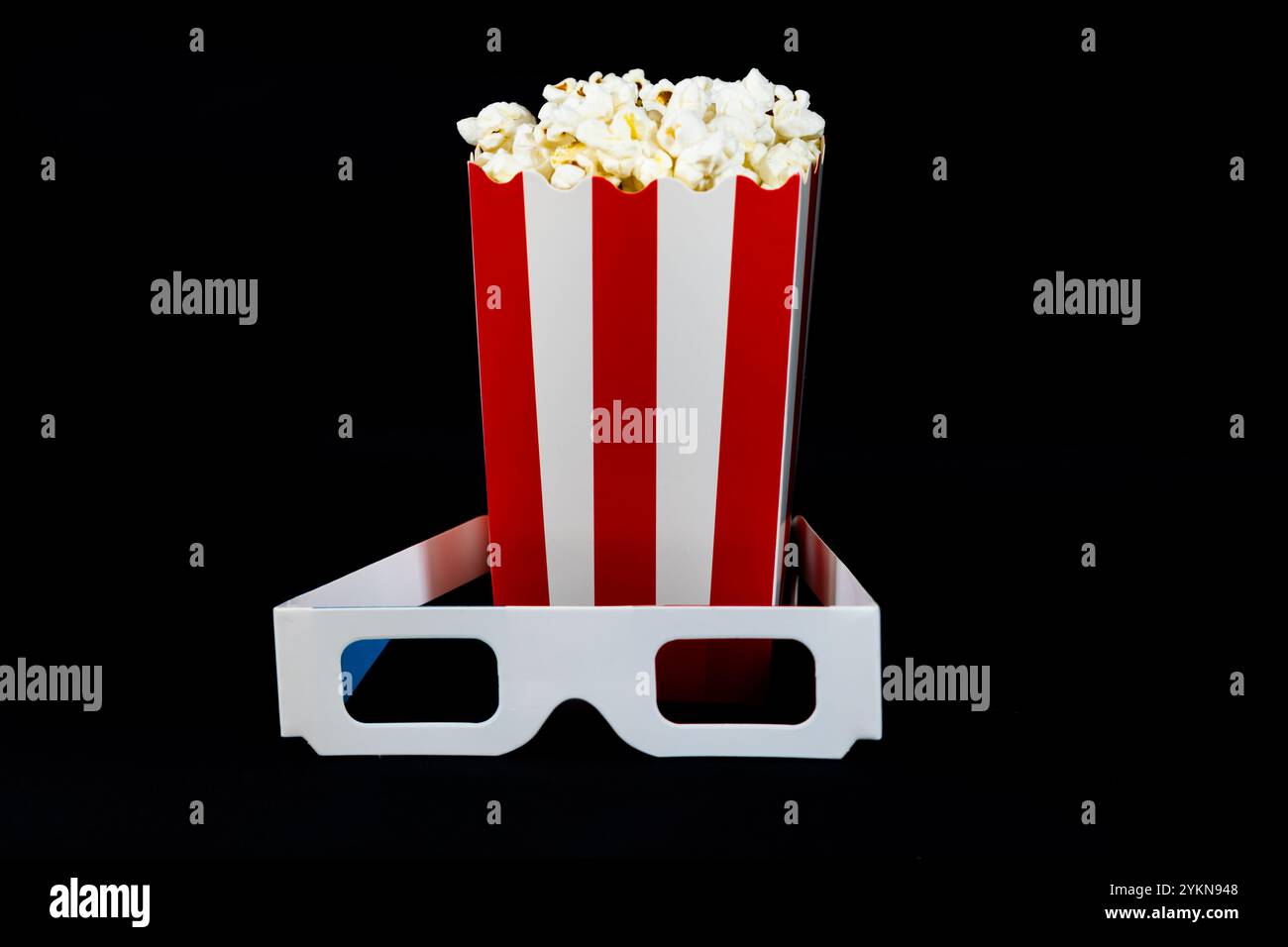 Popcorn in un secchio di cartone rosso e bianco con occhiali 3d su sfondo nero, cinema e popcorn Foto Stock