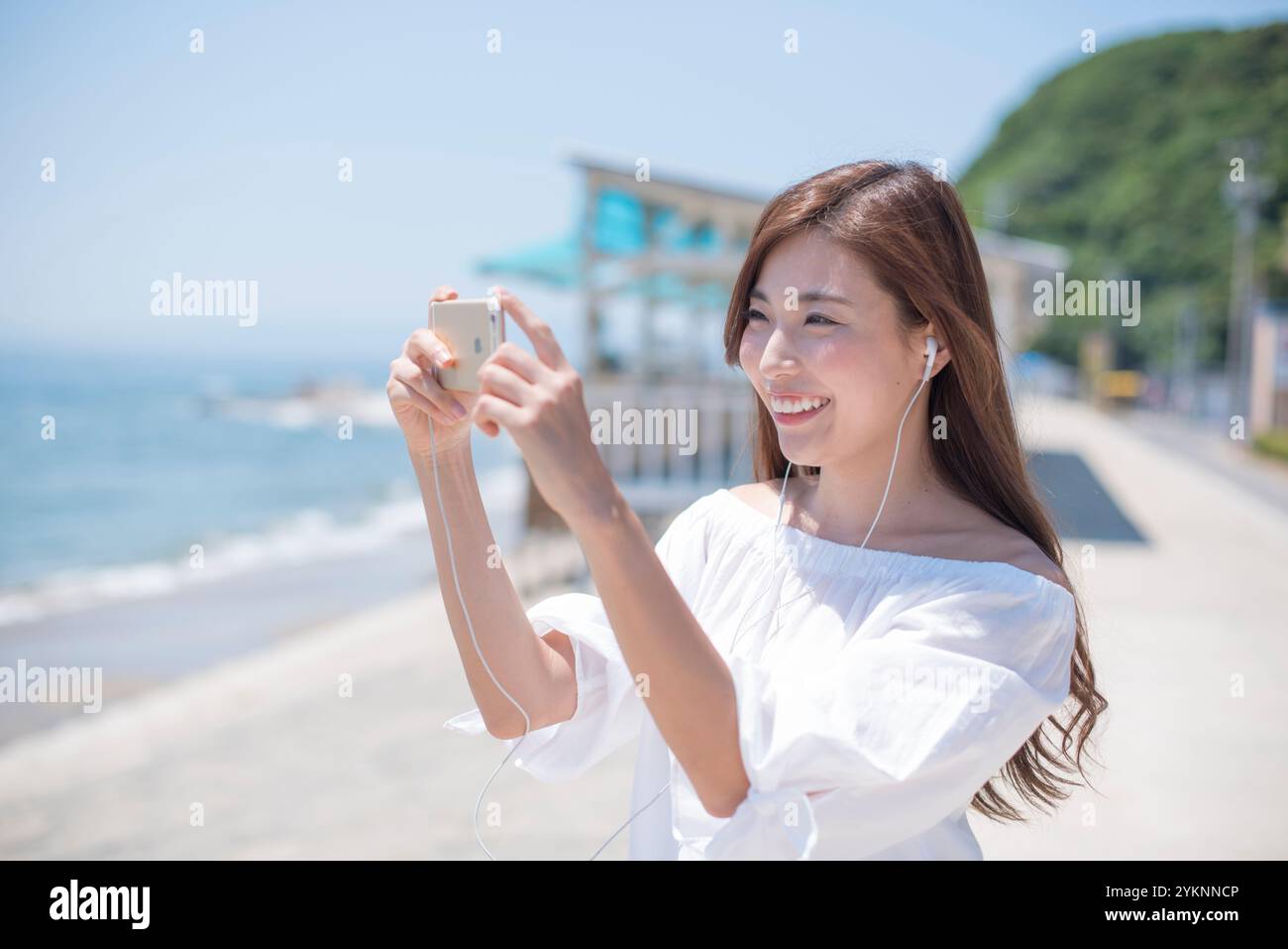 Donna che ascolta la musica sul telefono e scatta foto sulla riva del mare Foto Stock