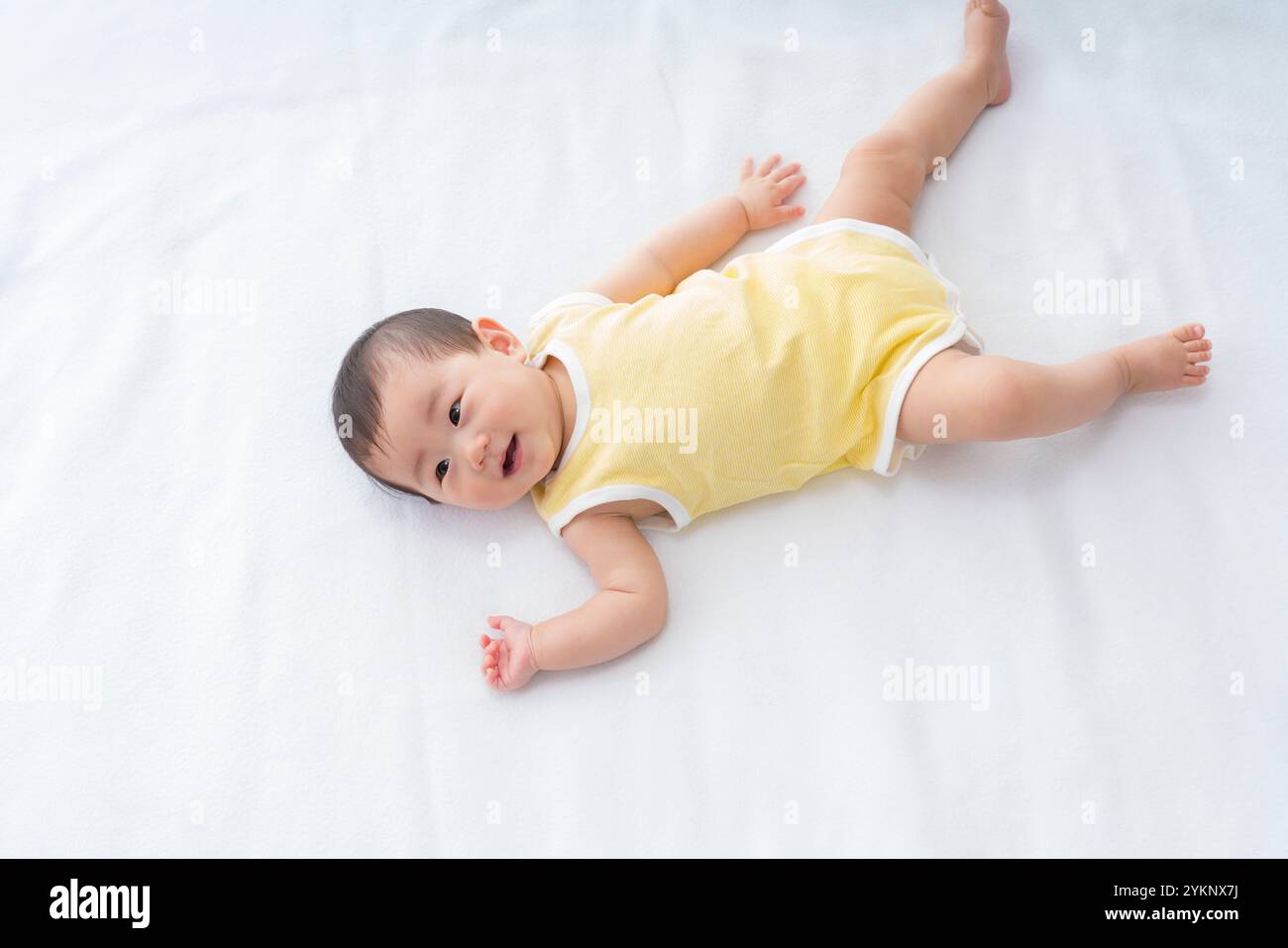 Bambino sospeso sdraiato e che gioca su un foglio bianco Foto Stock