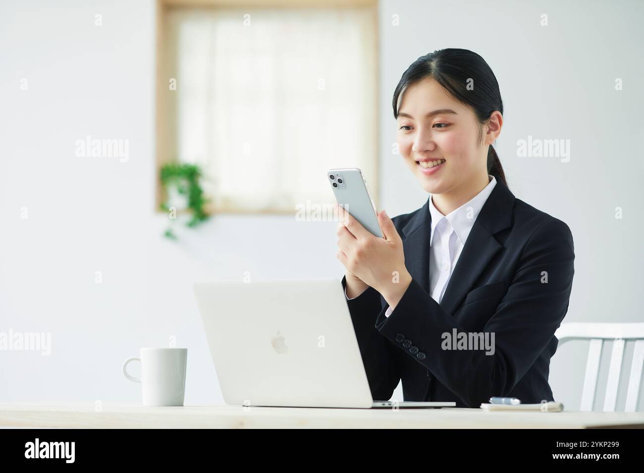 Giovane donna in costume che tiene lo smartphone davanti al computer portatile Foto Stock