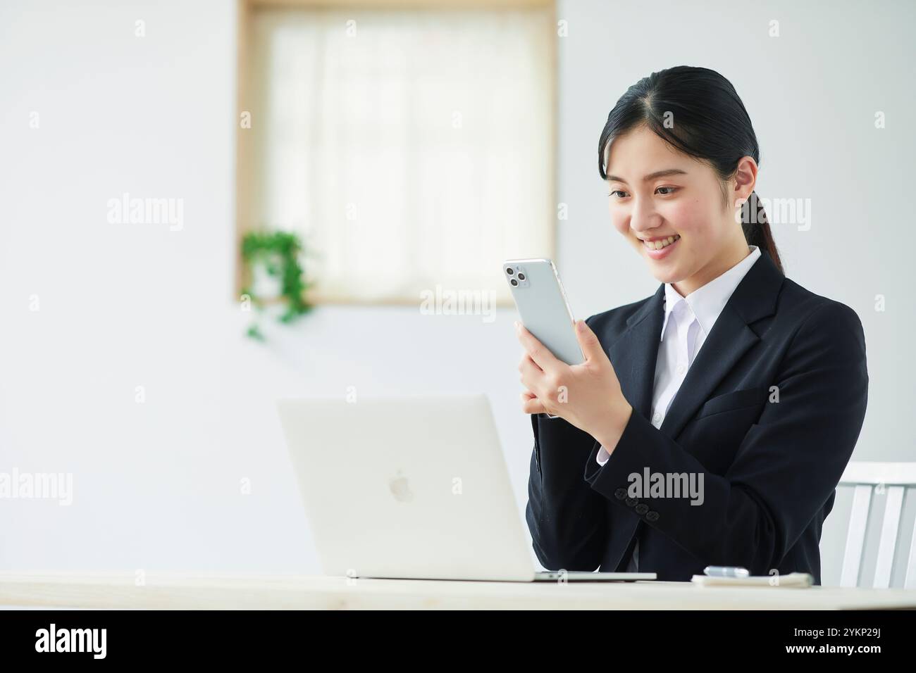 Giovane donna in costume che tiene lo smartphone davanti al computer portatile Foto Stock
