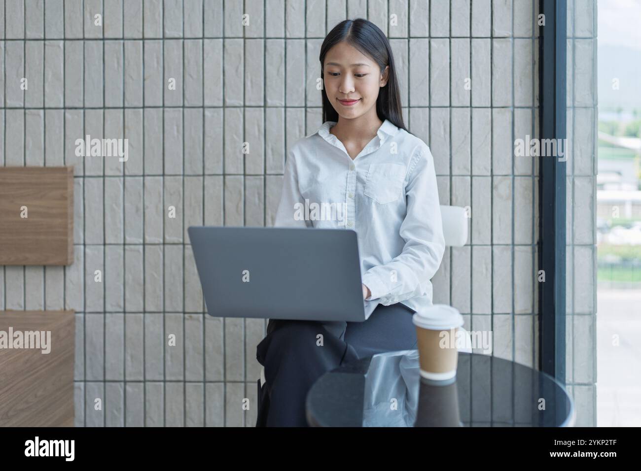 Una giovane donna è concentrata sul suo portatile in un elegante bar, sorseggiando un caffè e immergendosi nell'atmosfera rilassante creata dalla luce naturale. Foto Stock
