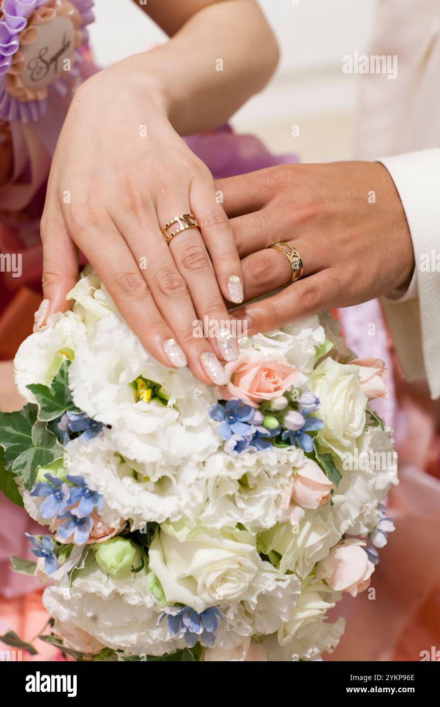 Sposa e sposo indossano fedi nuziali con bouquet mani alla cerimonia di nozze Foto Stock