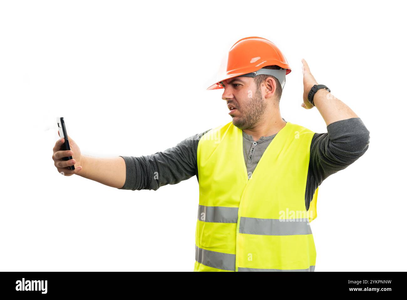 Uomo costruttore al lavoro che indossa il casco di sicurezza arancione e il gilet giallo fluorescente durante la videochiamata utilizzando lo smartphone isolato su sfondo bianco studio Foto Stock
