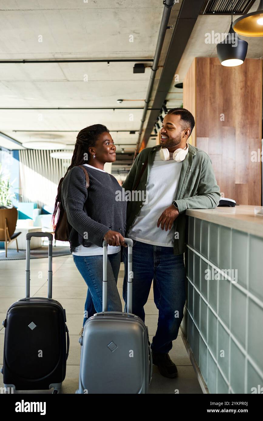 Una coppia gioiosa si trova nella lobby dell'hotel, preparandosi per la loro eccitante avventura di vacanza. Foto Stock