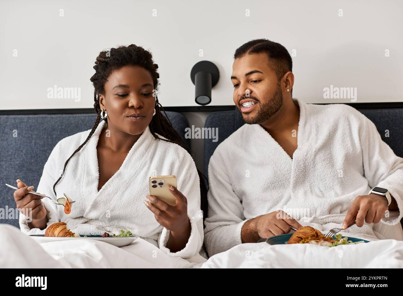 Una giovane coppia condivide risate e un pasto nella loro camera d'albergo mentre si godono le vacanze. Foto Stock
